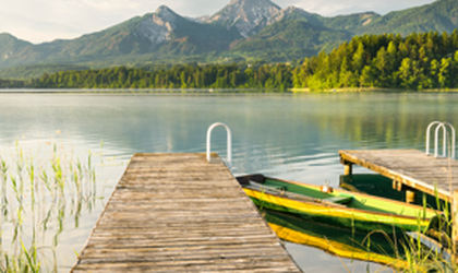 Ein Holzsteg führt zu einem gelb-grünen Ruderboot auf einem ruhigen See in Österreich, umgeben von Bergen.