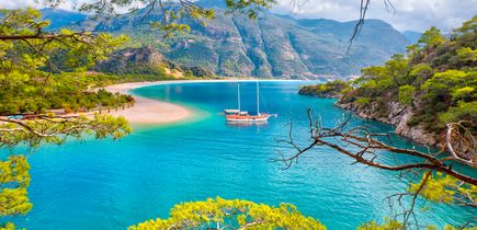 Atemberaubender Blick auf die Blaue Lagune von Ölüdeniz, Türkei, mit einem Segelboot im türkisblauen Wasser, umgeben von grünen Bergen und Pinienwäldern.