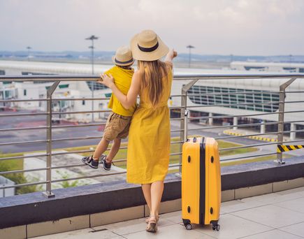 Frau und Kind in gelb mit gelbem Koffer am Flughafen