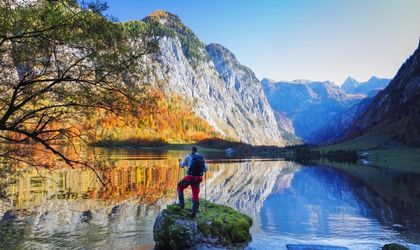 Eine Person steht auf einem Felsen im Königssee, Berchtesgaden, umgeben von herbstlichen Bergen und spiegelndem Wasser.