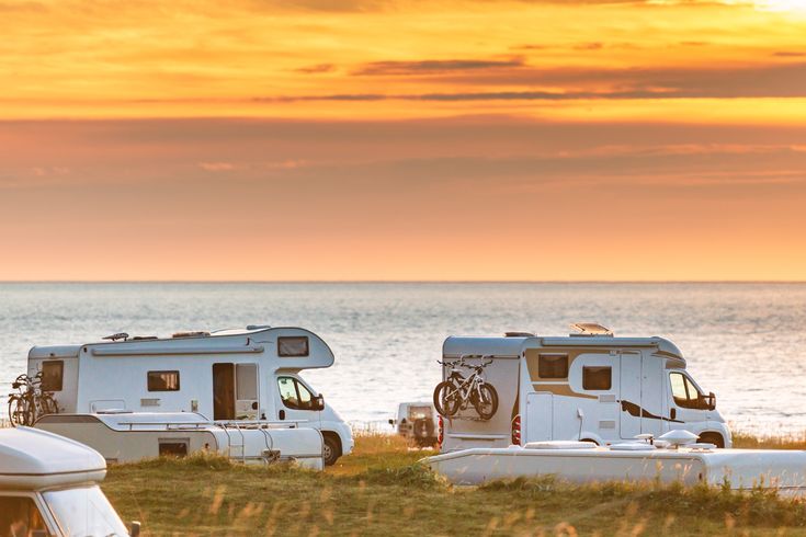 Weißer Campervan steht an einem Fjordufer in Norwegen bei Sonnenuntergang, umgeben von Bergen.