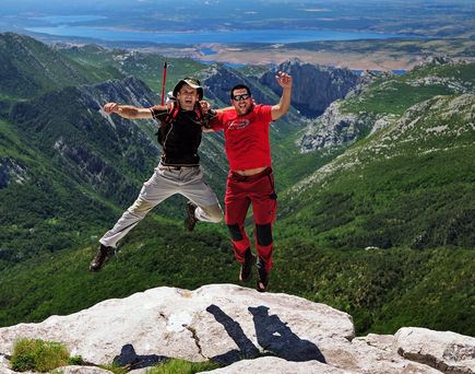 Zwei Personen springen in die Luft auf einer felsigen Klippe.