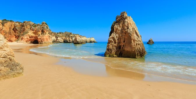 Strand an der Algarve. Blick über den Sand auf einen Felsen der aus dem Wasser ragt