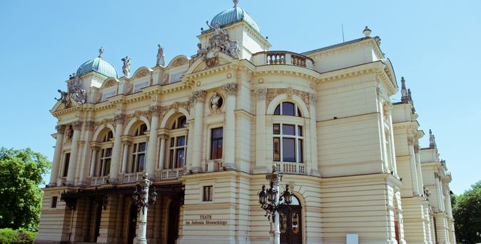 Zu sehen ist das Theater in Krakau. Ein großes weißes Gebäude mit ein paar Bäumen vor dem Eingang.