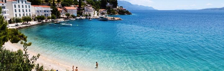 Ein Sandstrand mit türkisfarbenem Wasser, umgeben von grüner Vegetation.