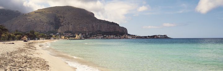 Ein Sandstrand mit türkisfarbenem Wasser, umgeben von Bergen.
