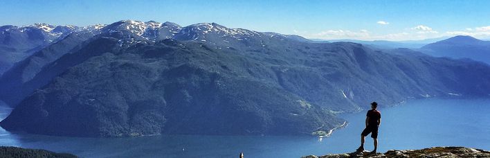 Eine Person steht auf einem Bergkamm und blickt über eine weite, bergige Landschaft in Norwegen.