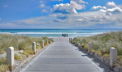 Ein Holzsteg führt über Dünen zum Sandstrand von Juliusruh auf Rügen, mit Meer und blauem Himmel.