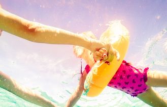 Mujtter und Kind im rosa Badeanzug und gelbem Schwimmreifen.