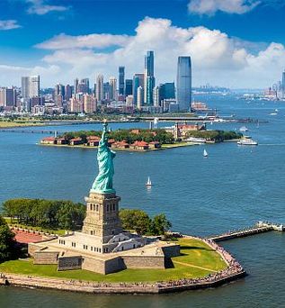 Die Freiheitsstatue auf Liberty Island in New York, USA, erhebt sich majestätisch vor der Skyline von Manhattan und dem blauen Himmel.
