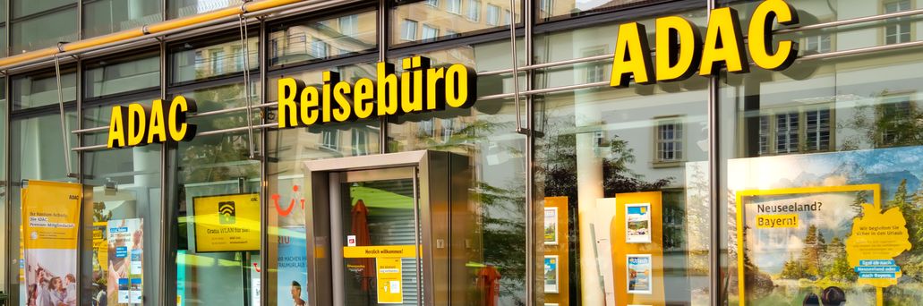 ADAC Reisebüro mit gläserner Fassade und gelber Beschriftung in einer Innenstadtlage, Schaufenster mit Urlaubsangeboten.