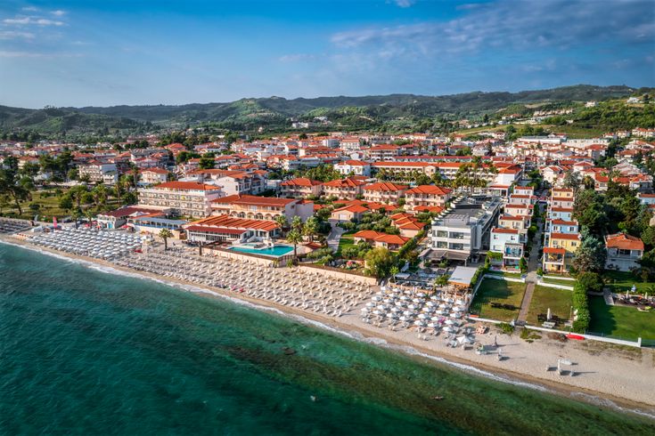 Blick auf Hanioti aus der Vogelperspektive. Breiter Strand mit Liegen, dahinter Grün und Häuser.