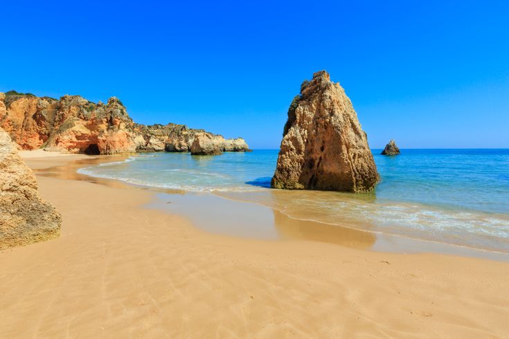 Strand an der Algarve. Blick über den Sand auf einen Felsen der aus dem Wasser ragt