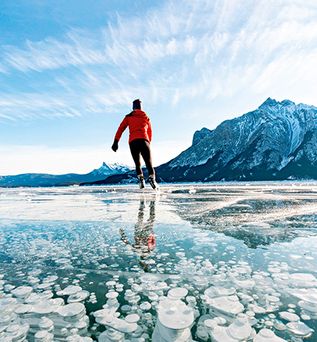 Eisläufer in Kanada auf einem See mit Bergen im Hintergrund