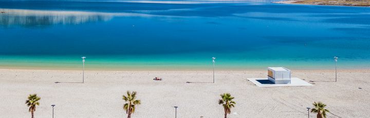 Ein Sandstrand mit Strandliegen und türkisfarbenem Wasser.