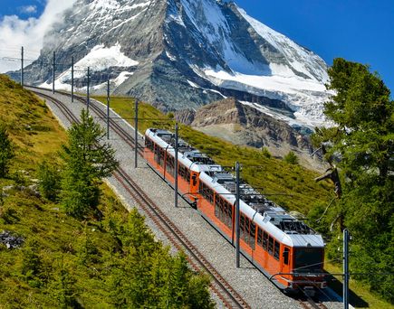 Eine Zahnradbahn fährt auf einem Gleis, das sich einen Berg hinaufschlängelt, mit dem Matterhorn im Hintergrund.