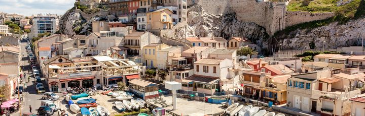 Eine malerische Küstenstadt mit vielen Booten, die im Hafen liegen. Die Häuser sind in warmen Farben gehalten und schmiegen sich an den Hang, während sich das Meer bis zum Horizont erstreckt.