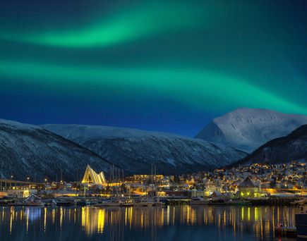 Die Nordlichter in grünem Licht über einer norwegischen Küstenstadt in der Nacht.