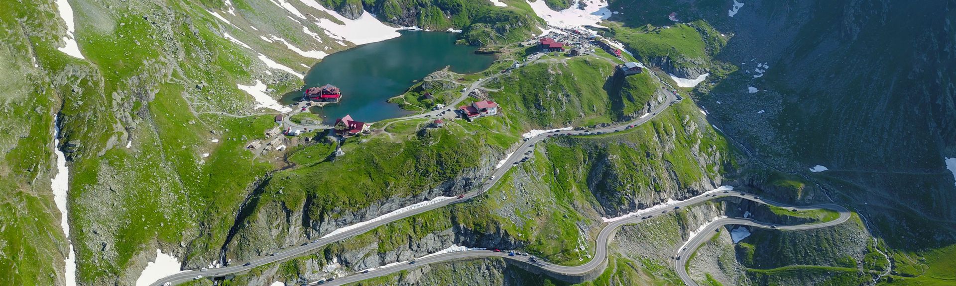 Luftaufnahme des Kessels des Balea-Sees, des steilen Fagaras-Gebirges und der Transfagarasan-Straße, die sich entlang der felsigen Klippen der Berge schlängelt. Karpaten, Rumänien