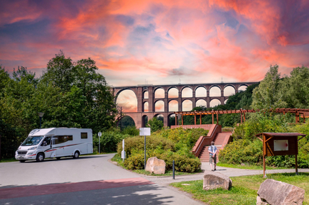 Camper steht an einer Straße in Deutschland im Hintergrund historische Brücke