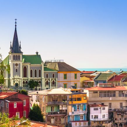 Das historische Viertel von Valparaíso, Chile, mit seinen bunten Häusern an steilen Hängen, die sich zum Meer hinunterziehen, und einem großen Wandgemälde auf einer Mauer.