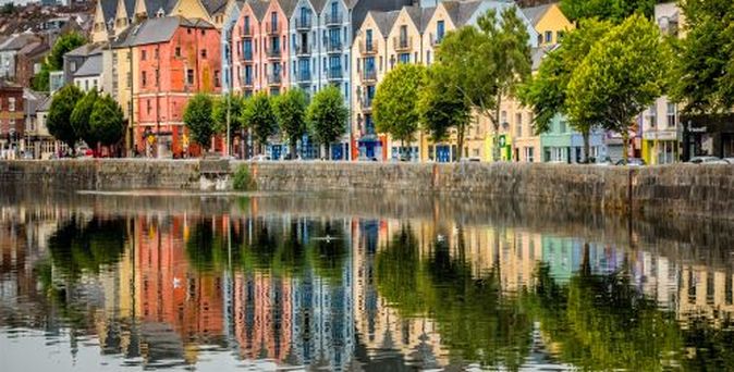 Eine Stadtansicht von Cork mit bunten Gebäuden, die sich im Fluss spiegeln.