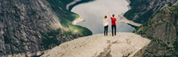 Eine Person steht auf der Trolltunga-Felsformation und blickt auf eine weite Landschaft.