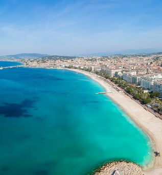 Die Promenade de la Croisette in Cannes, Frankreich, mit dem breiten Sandstrand, dem blauen Mittelmeer und den luxuriösen Hotels und Palmen entlang der Küste.
