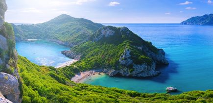 Die Doppelbucht von Porto Timoni auf Korfu, Griechenland, mit zwei Stränden, die von üppiger grüner Vegetation und steilen Klippen umgeben sind, während das blaue Meer im Hintergrund liegt.