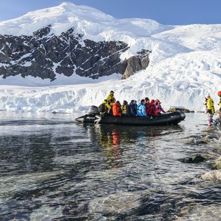 Ein Schlauchboot mit Passagieren nähert sich einer eisigen Küste mit Eisbergen.