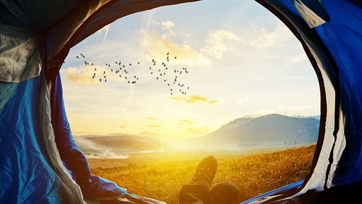 Blick aus einem Zelt auf eine sonnenbeschienene Landschaft mit See und Bergen.