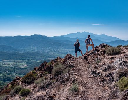 Zwei Personen wandert auf einem Bergpfad mit Blick auf eine weite Landschaft.