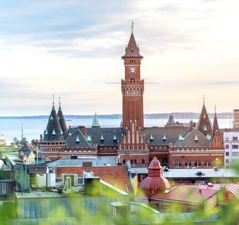 Blick auf die Stadt Helsingborg mit seinem Kirchturm und einigen Häusern. Im Hintergrund ist Wasser zu sehen.