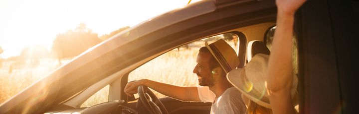 Eine Person fährt Auto, mit Surfbrettern auf dem Dach, bei Sonnenuntergang.