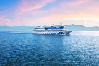 Klippe mit Ortschaft am Meer, im Hintergrund Berge 