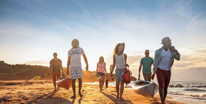Mehrere Menschen tragen Kanus am Strand entlang, zum Sonnenuntergang