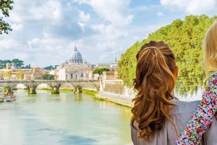 Frau mit Kind auf dem Arm blicken am Fluss auf den Petersdom in Rom 