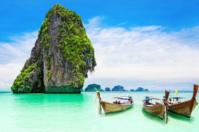 3 typisch thailändische Boote vor Felsen an einer Küste in Thailand