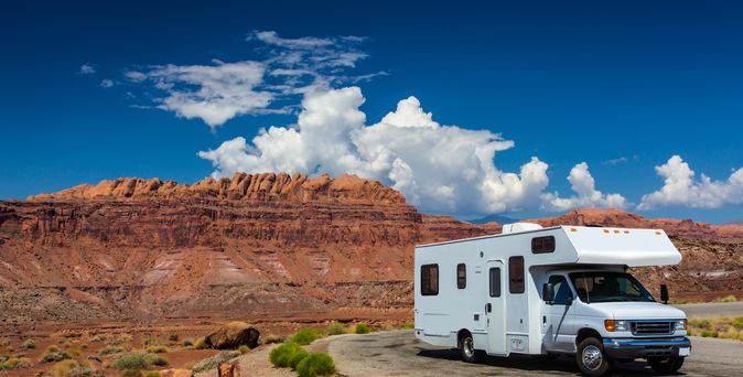 Weißer Campervan parkt auf einer Straße in einem Canyon mit roten Felsen unter blauem Himmel.