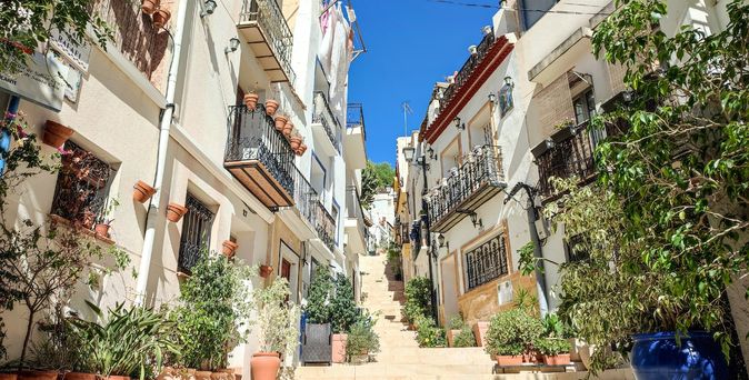 Eine enge Gasse in einer mediterranen Stadt mit bunten Gebäuden und Blumen.