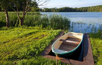 Ein kleines Ruderboot liegt am Ufer eines ruhigen Sees mit Schilf und Gras.