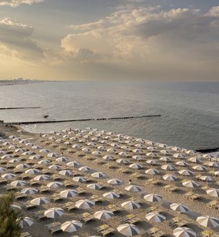 Reihenweise Sonnenschirme und Liegen an einem ruhigen Sandstrand bei Sonnenuntergang mit Blick auf das Meer.