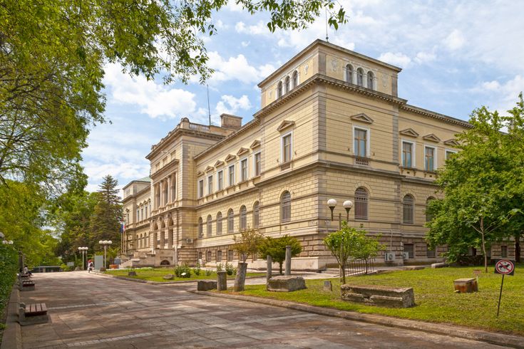 Archäologisches Museum in Varna, Blick von der Straße auf das hübsche Gebäude. Weg ist mit Gras und Bäumen geebnet.