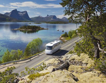 Weißer Campervan steht an einem Fjordufer in Norwegen bei Sonnenuntergang, umgeben von Bergen.