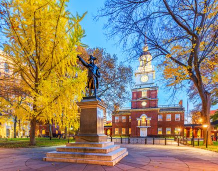 Independence Hall in Philadelphia mit Statue davor und farbenprächtigen Bäumen