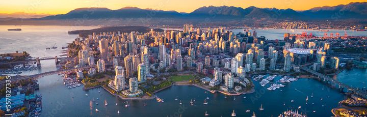 Eine beeindruckende Luftaufnahme der Stadt Vancouver, Kanada, mit ihrer Skyline, die sich an der Küste erstreckt, umgeben von Bergen und Wasser unter einem weiten Himmel.