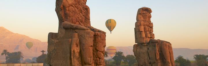 Die zwei kolossalen Statuen der Memnonkolosse, die majestätisch in der Landschaft stehen und die Überreste eines antiken Tempels markieren.