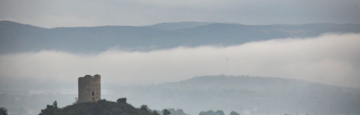 Eine alte Burgruine auf einem Hügel, umgeben von grünen Bergen.