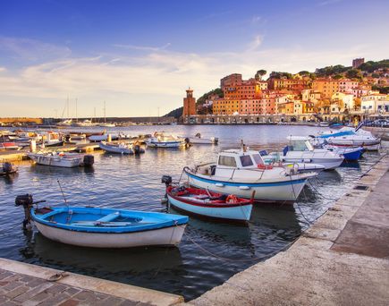 Malerischer Hafen von Rio Marina auf Elba mit bunten Fischerbooten und Häusern am Ufer bei Sonnenuntergang.