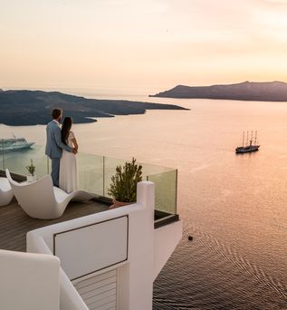 Paar steht auf dem Balkon eines griechischen Luxushotels und blickt im Sonnenuntergang auf das Meer 